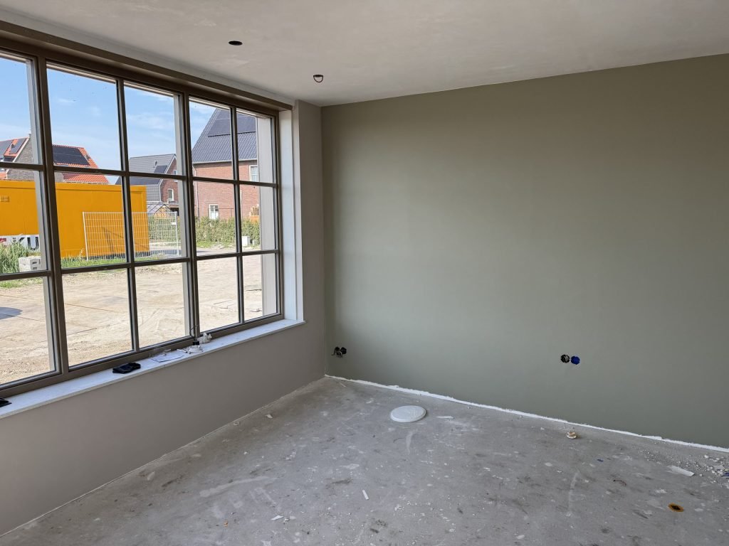 Egaal gesausde wand in een grijsgroene tint, met daglicht dat door een groot raam naar binnen valt
