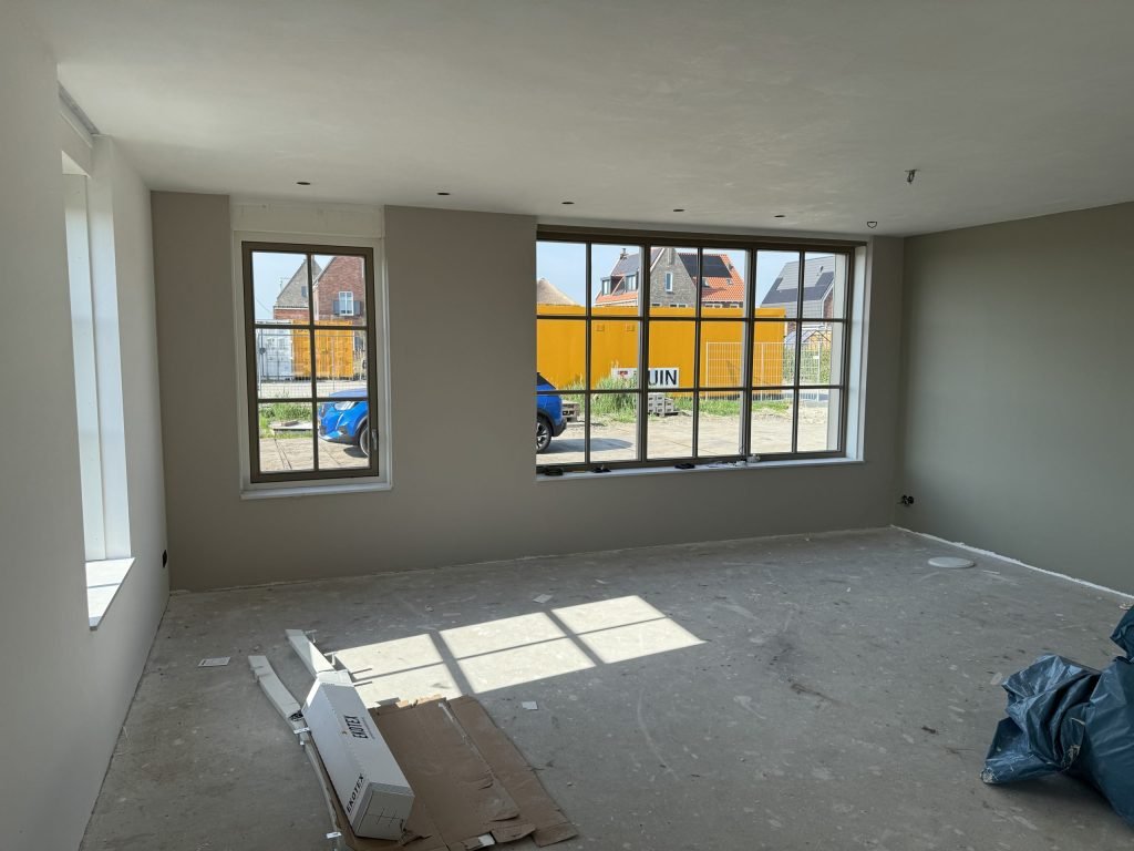 Nieuwbouwkamer met lichte wanden en grote ramen waardoor het daglicht schuin binnenvalt