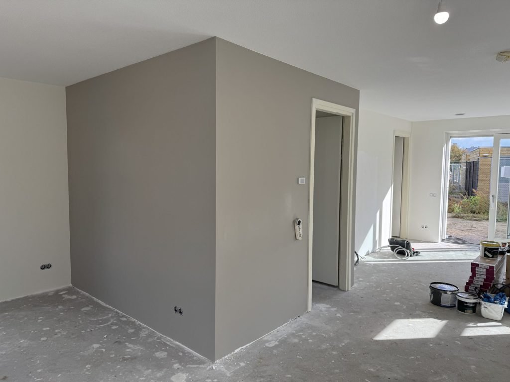 Pas gesausde grijze wand in een nieuwbouwwoning met verfemmers op de vloer
