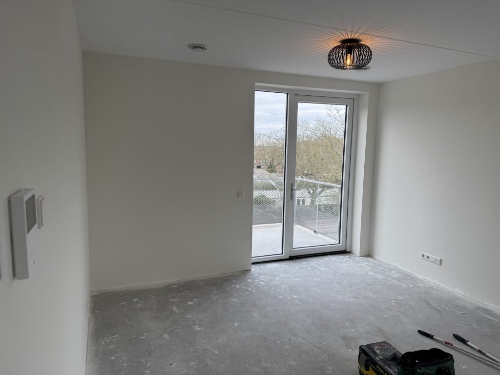 Lege nieuwbouwkamer met openslaande deuren en strakke witte wanden, kort na de oplevering
